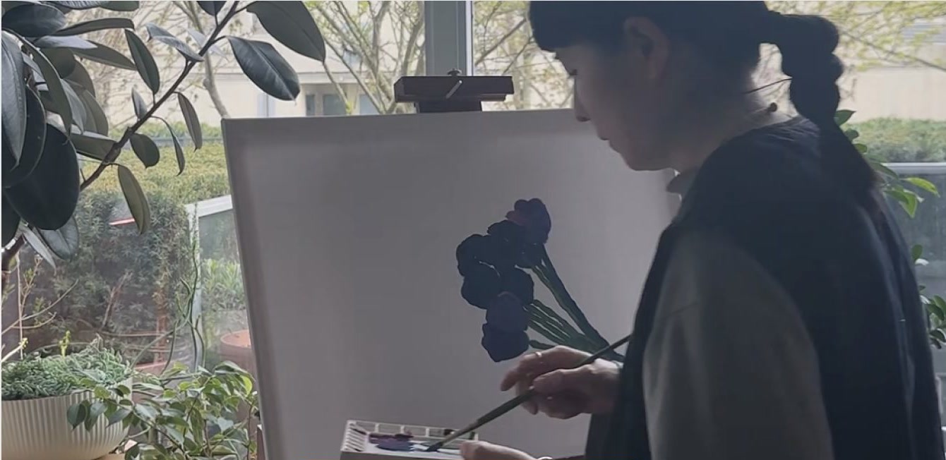 Wendi painting at an easel beside a window and plants