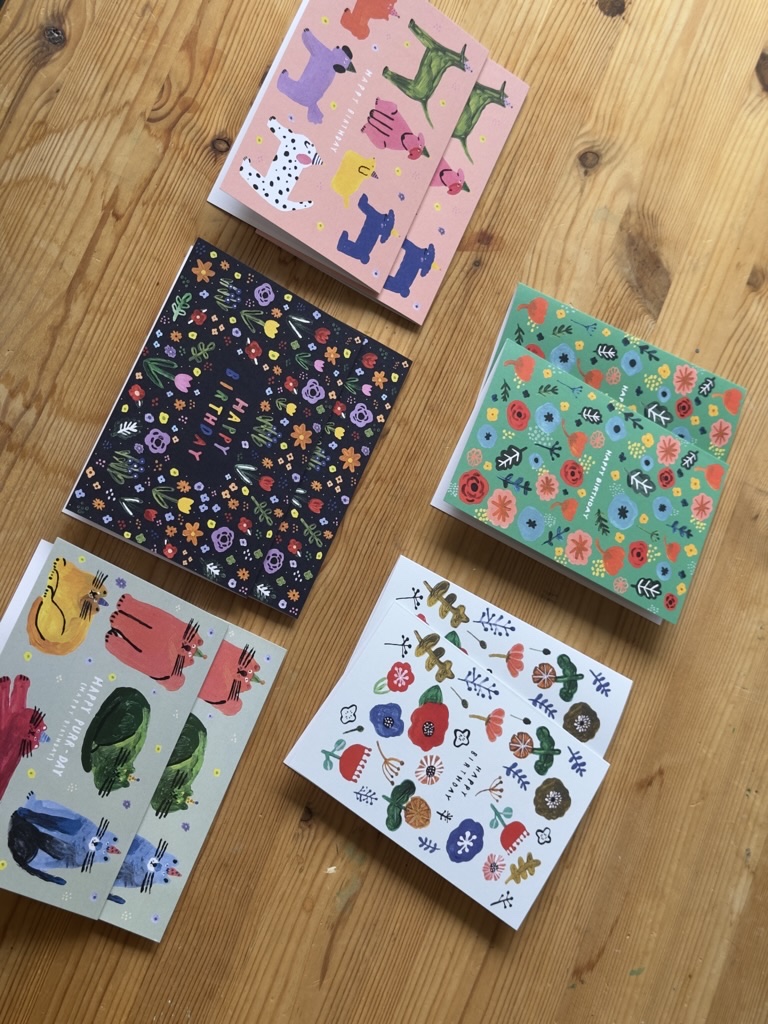 Ten illustrated Birthday Friends greeting cards arranged on a wooden table.