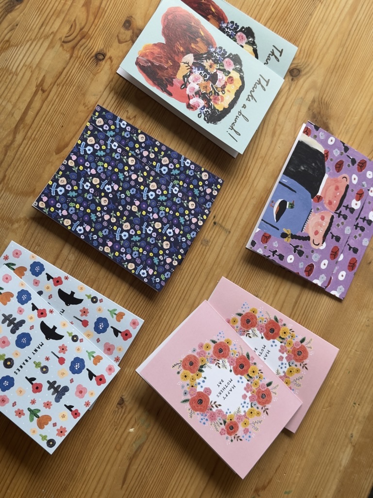 Ten illustrated Flower Notes greeting cards arranged on a wooden table.