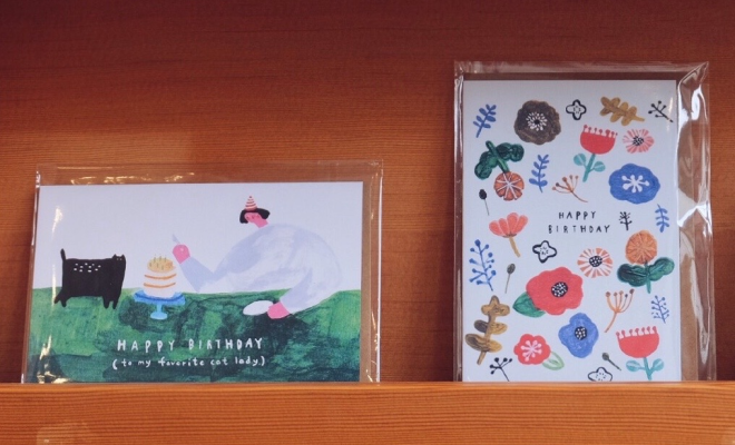 Two colourful Babincho greeting cards displayed on a wooden shelf